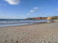 a sandy beach in front of a cliff and ocean with sand on the ground and the waves rolling