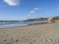 a sandy beach in front of a cliff and ocean with sand on the ground and the waves rolling