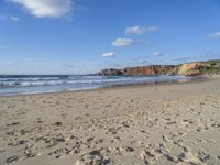 a sandy beach in front of a cliff and ocean with sand on the ground and the waves rolling