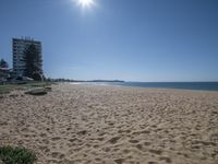 footprints in the sand on a sandy beach overlooking a ocean and apartment buildings with a clear sky