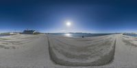 fisheye panorama of a sandy beach and a sun rise over mountains in the distance