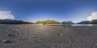 a panorama of a sandy beach with a blue sky in the background and mountains in the background