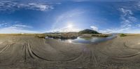 the fisheye photo shows a sandy beach and mountains with a river running through it