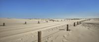 a fence on a sandy beach next to the ocean and sand dunes in the distance