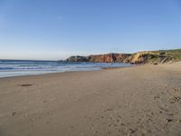 a wide sandy beach with footprints of people walking in the water and cliff cliffs near the ocean