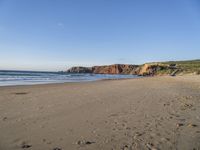 a wide sandy beach with footprints of people walking in the water and cliff cliffs near the ocean