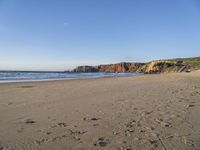 a wide sandy beach with footprints of people walking in the water and cliff cliffs near the ocean