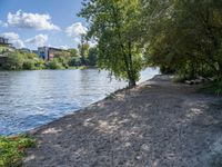 a sandy beach with trees in the background next to some water and a city building