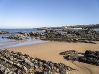 a lone sandy beach with rocks and water around it on a sunny day with clear sky