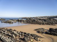 a lone sandy beach with rocks and water around it on a sunny day with clear sky