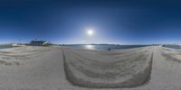 fisheye panorama of a sandy beach and a sun rise over mountains in the distance