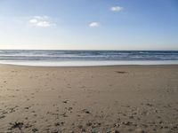 a person is sitting down on a sandy beach by the ocean at sunset, with their feet in the sand