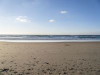 a person is sitting down on a sandy beach by the ocean at sunset, with their feet in the sand