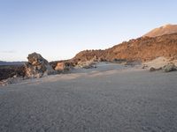 an empty sandy beach with boulders in the background in the evening light, with the sun setting behind the hill and the rock formations