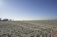 people walk on sand at a beach, near the ocean in the distance is a sky with few cloudless, and blue skies