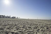 people walk on sand at a beach, near the ocean in the distance is a sky with few cloudless, and blue skies