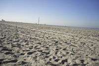 people walk on sand at a beach, near the ocean in the distance is a sky with few cloudless, and blue skies