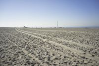 people walk on sand at a beach, near the ocean in the distance is a sky with few cloudless, and blue skies