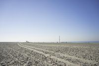 people walk on sand at a beach, near the ocean in the distance is a sky with few cloudless, and blue skies