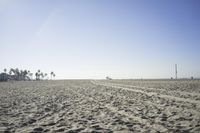 people walk on sand at a beach, near the ocean in the distance is a sky with few cloudless, and blue skies