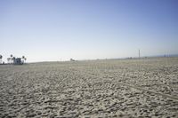 people walk on sand at a beach, near the ocean in the distance is a sky with few cloudless, and blue skies
