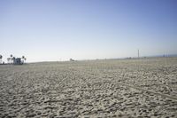 people walk on sand at a beach, near the ocean in the distance is a sky with few cloudless, and blue skies