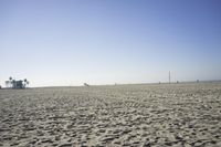 people walk on sand at a beach, near the ocean in the distance is a sky with few cloudless, and blue skies