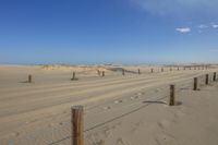 sand duned beach with fence and poles on sunny day with blue sky and clouds