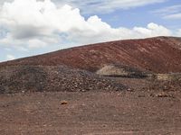 a horse is grazing on the flat land near some rocks and a hill and clouds