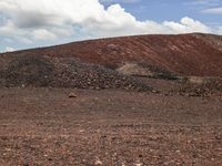 a horse is grazing on the flat land near some rocks and a hill and clouds