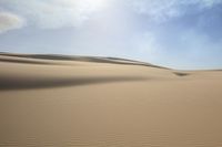 a field filled with sandy and sparse dunes in the middle of a desert plain with a blue sky