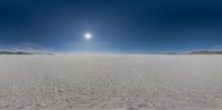 a panoramic view of a sandy area with snow and mountains in the background