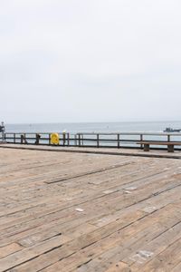 the wooden floor of a pier with a yellow surf board in the water behind it