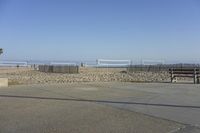 benches are lined up on the shore near a sandy beach area with a volleyball net, volleyball ball and benches are seen on the side