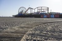 an empty beach area with sand and a ferris wheel in the background of the photo