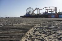 an empty beach area with sand and a ferris wheel in the background of the photo