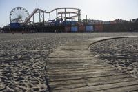 an empty beach area with sand and a ferris wheel in the background of the photo