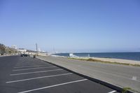 the view of a beach from inside an empty parking lot by the ocean as cars drive along it