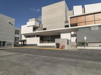 a parking lot with a cement building and an asphalt parking area beside it has many windows