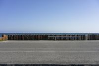 a wooden fence surrounds a parking lot with benches next to it by the ocean and on a sunny day