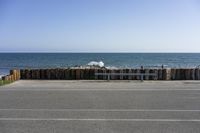 a wooden fence surrounds a parking lot with benches next to it by the ocean and on a sunny day