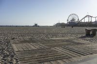 a boardwalk with benches, amusement ride wheel and wooden boards in front of an empty beach