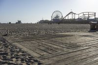 a boardwalk with benches, amusement ride wheel and wooden boards in front of an empty beach