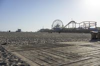 a boardwalk with benches, amusement ride wheel and wooden boards in front of an empty beach