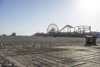 a boardwalk with benches, amusement ride wheel and wooden boards in front of an empty beach