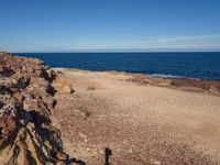 an open area with a dirt path leading the ocean to a shore that has some rocks and some water