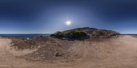 a lone beach at the edge of the water and rocks, in front of the sun