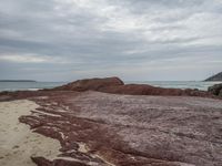 an orange and red rock sitting on top of a sandy beach near the ocean in low light