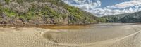 a small sandy beach sitting next to a river and forest covered hillsides in the background