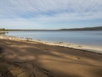 the view of water from an empty beach near a forest area and hill range in the distance